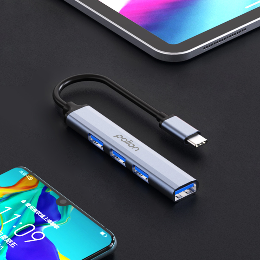 Szary hub USB-C z trzema niebieskimi portami USB, obok smartfona i tabletu.