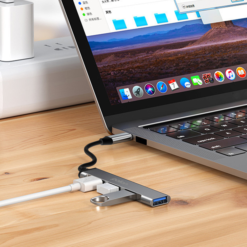 Szary koncentrator USB podłączony do laptopa z białymi kablami.
