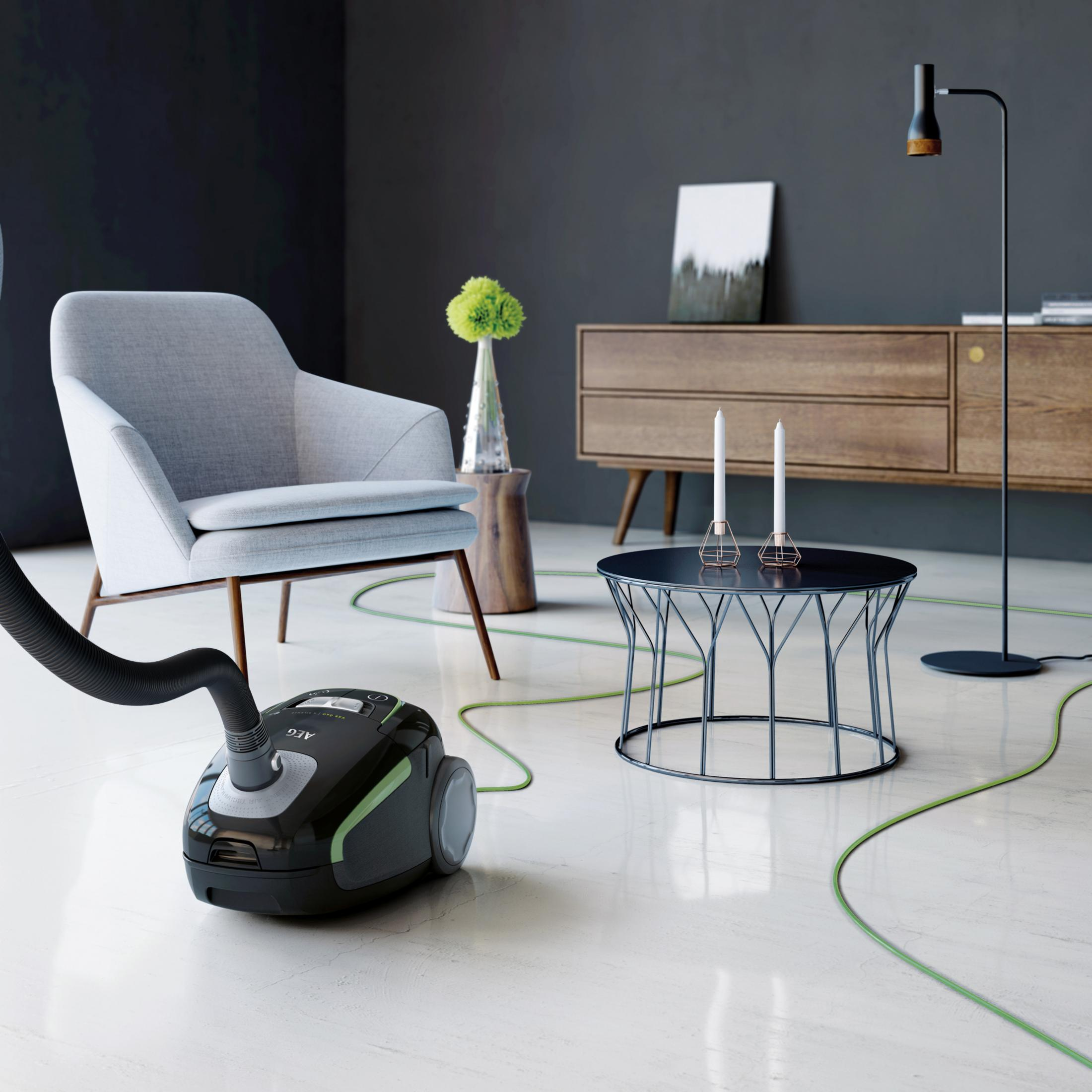 Una aspiradora negra con manguera verde en una sala de estar moderna.