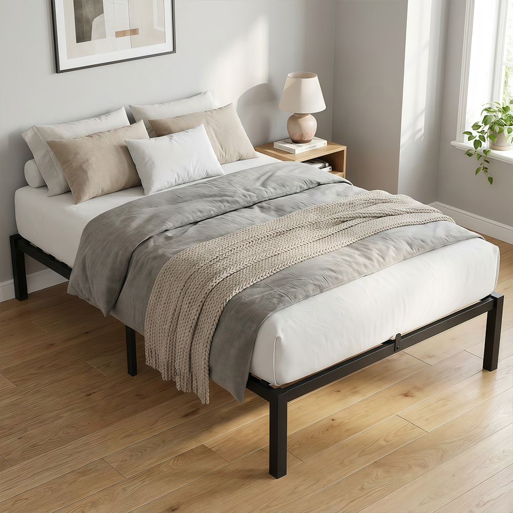 Ein Bett mit schwarzem Metallgestell und grauer Decke, Kissen, Nachttisch und Lampe.