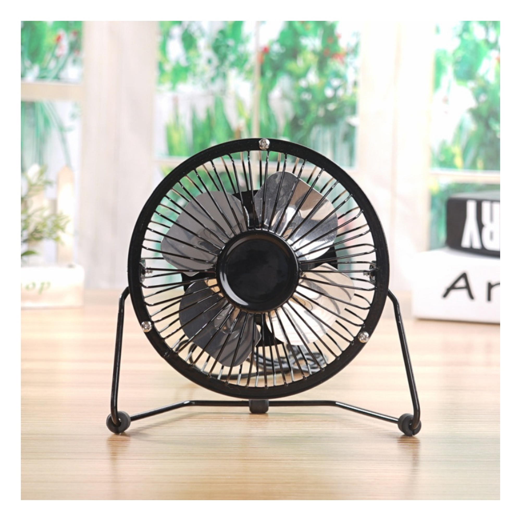 Ein kleiner schwarzer Ventilator mit Metallgitter steht auf einem Holztisch.