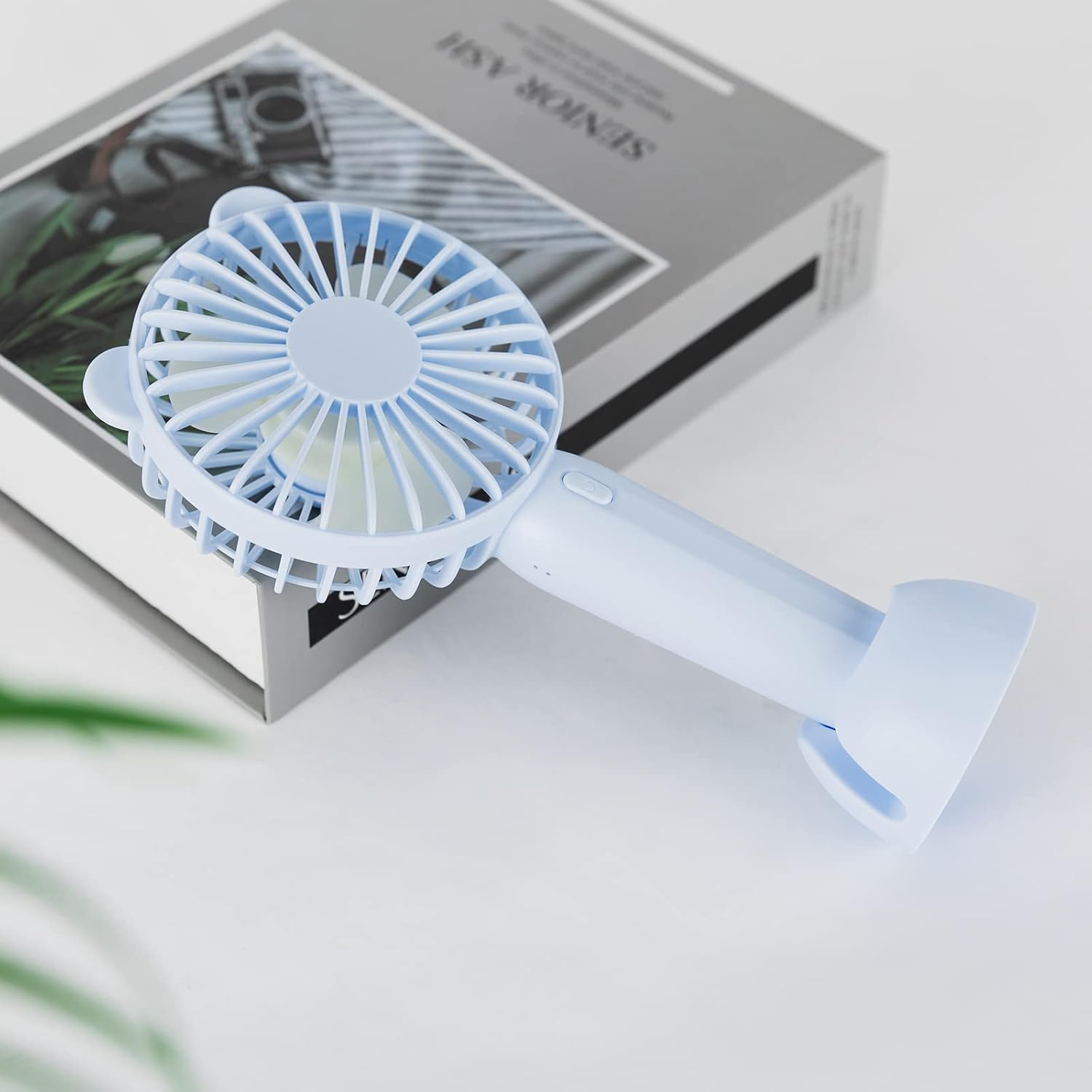 Ein hellblauer Handventilator liegt auf einem Buch.