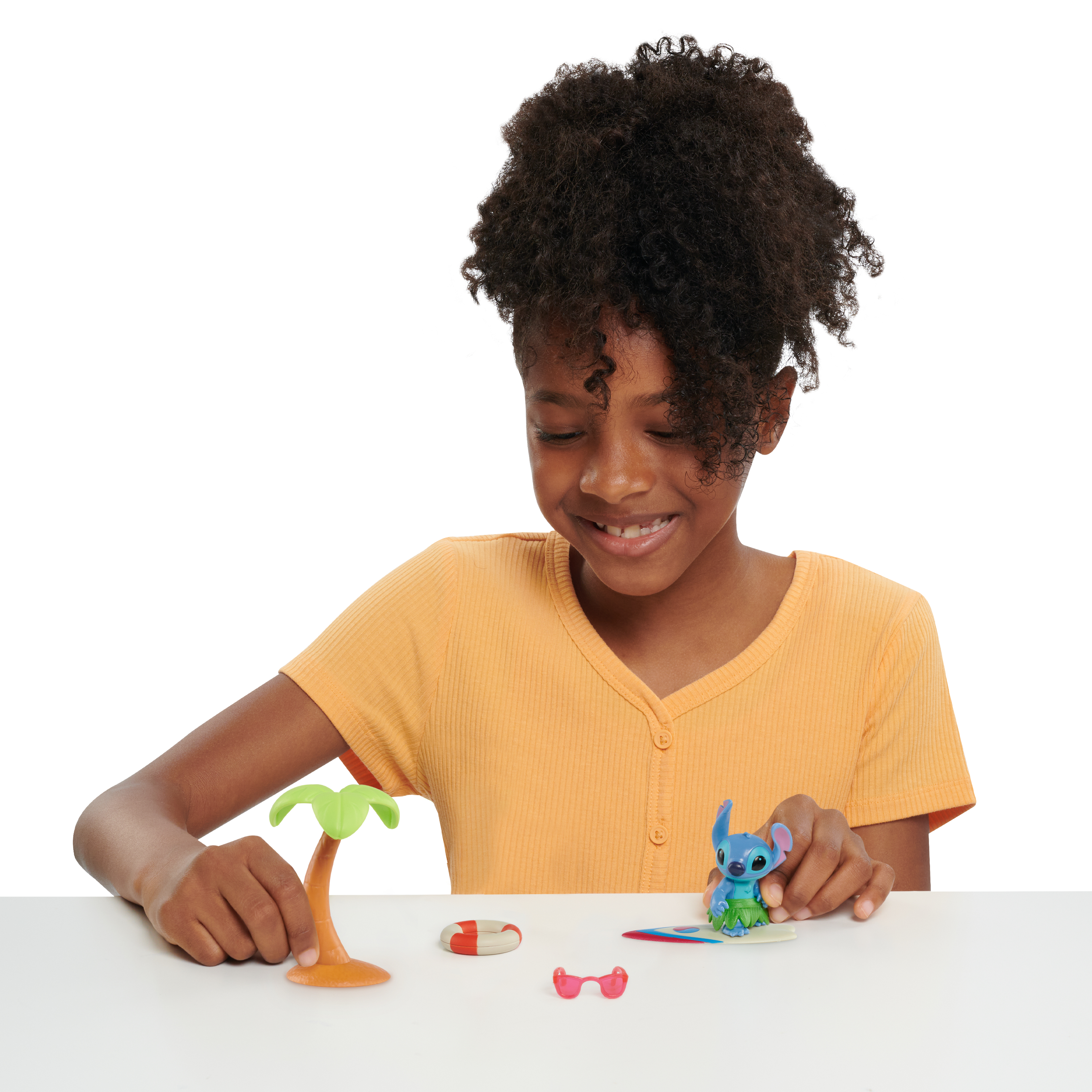 Una bambina gioca con una figura di Stitch, tavola da surf e giocattoli tropicali.