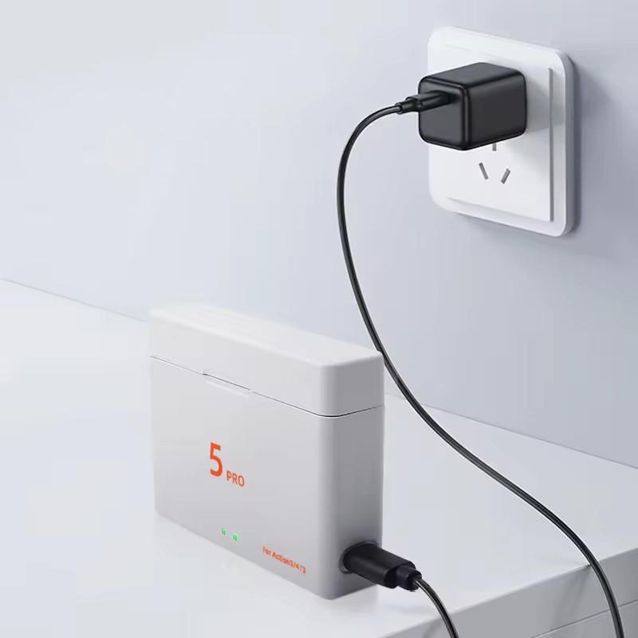 Eine weiße Box mit der Aufschrift 5 PRO lädt über ein schwarzes Kabel, das an einen schwarzen Netzstecker angeschlossen ist.