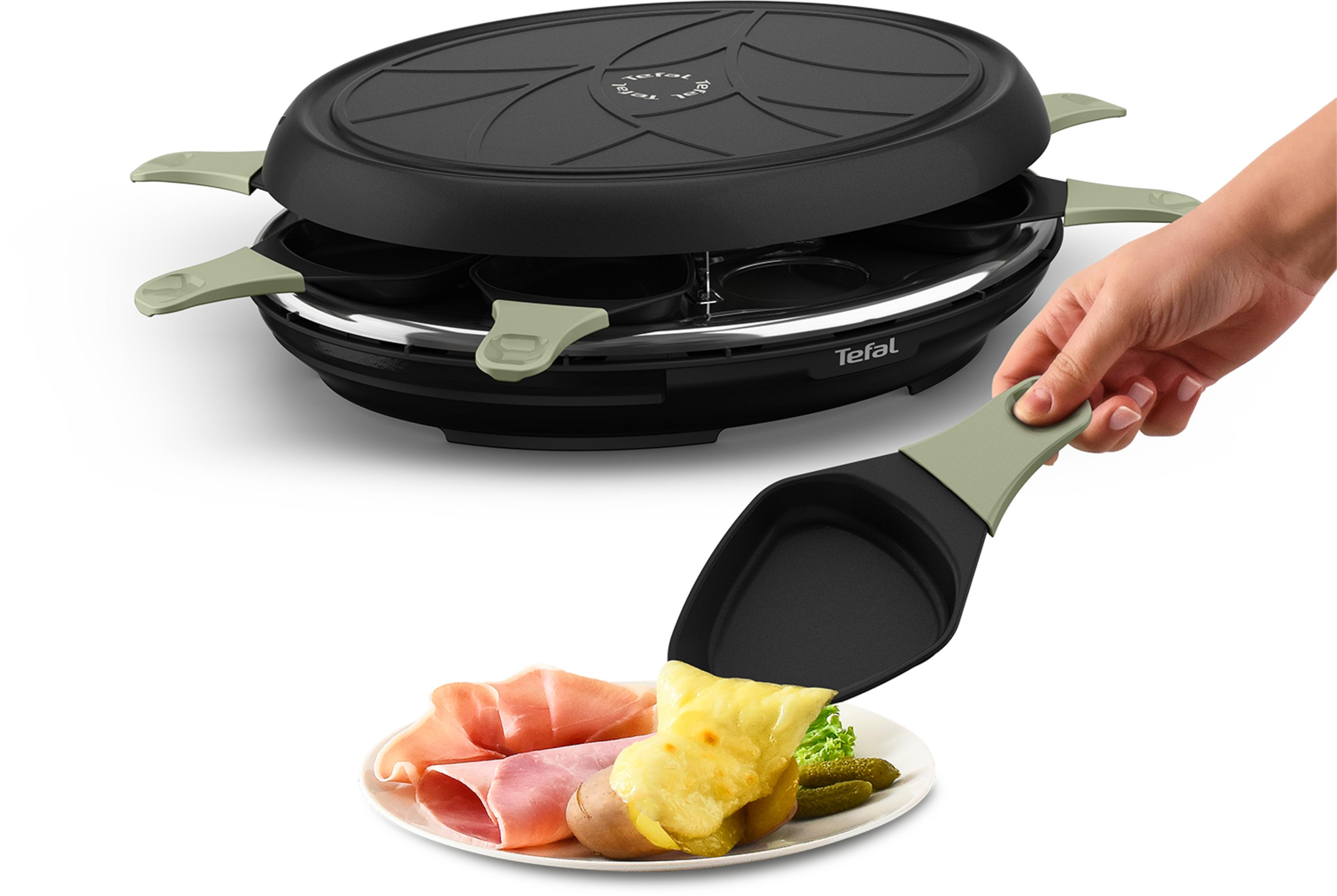 Grill per raclette con padelle e una spatola che mette il formaggio su un piatto con prosciutto e cetriolini.