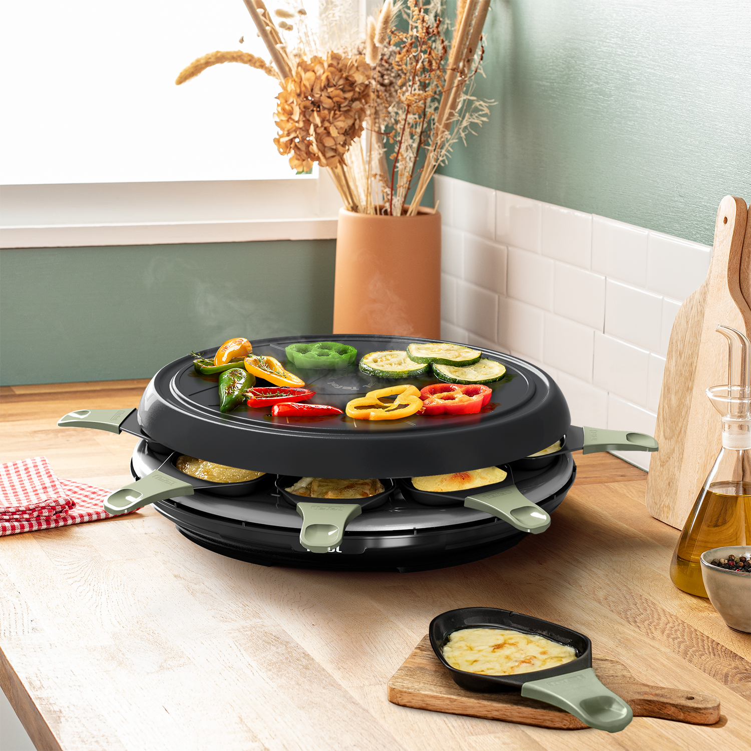 Grill da raclette con verdure e padelline al formaggio su tavolo legno.
