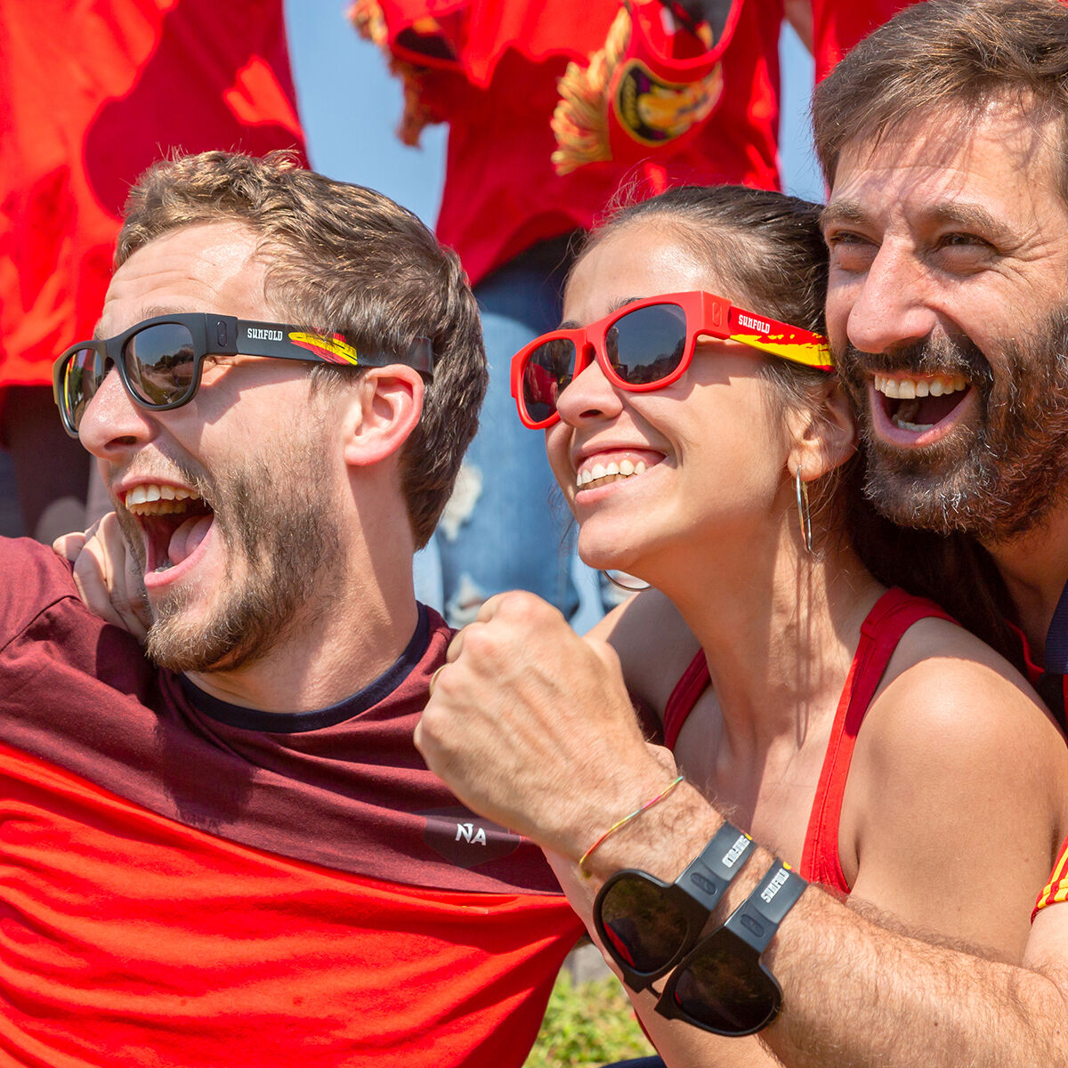 Drei lachende Fans in Rot mit Sonnenbrillen, die jubeln.