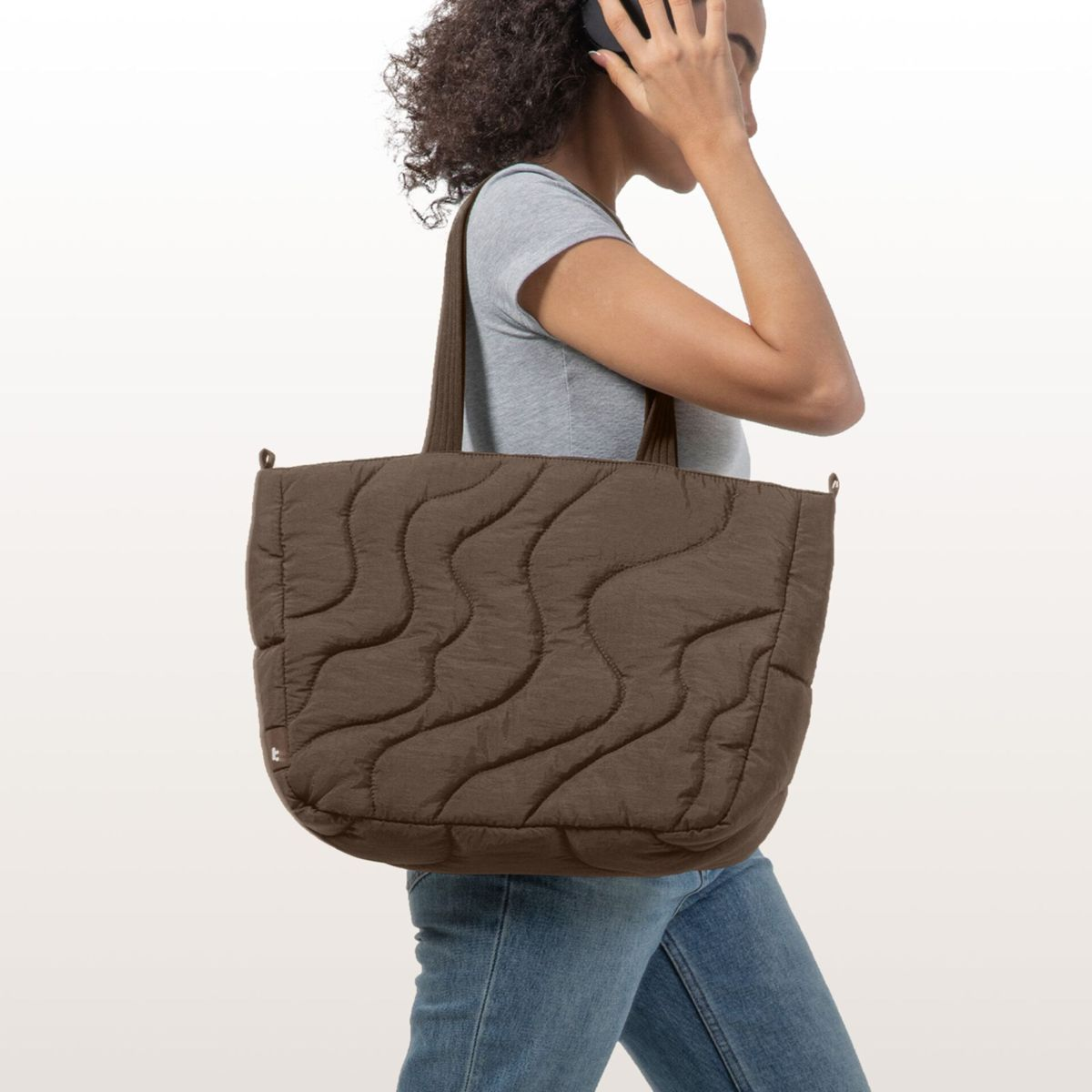 Vrouw met koptelefoon draagt een gewatteerde bruine tas en spijkerbroek.