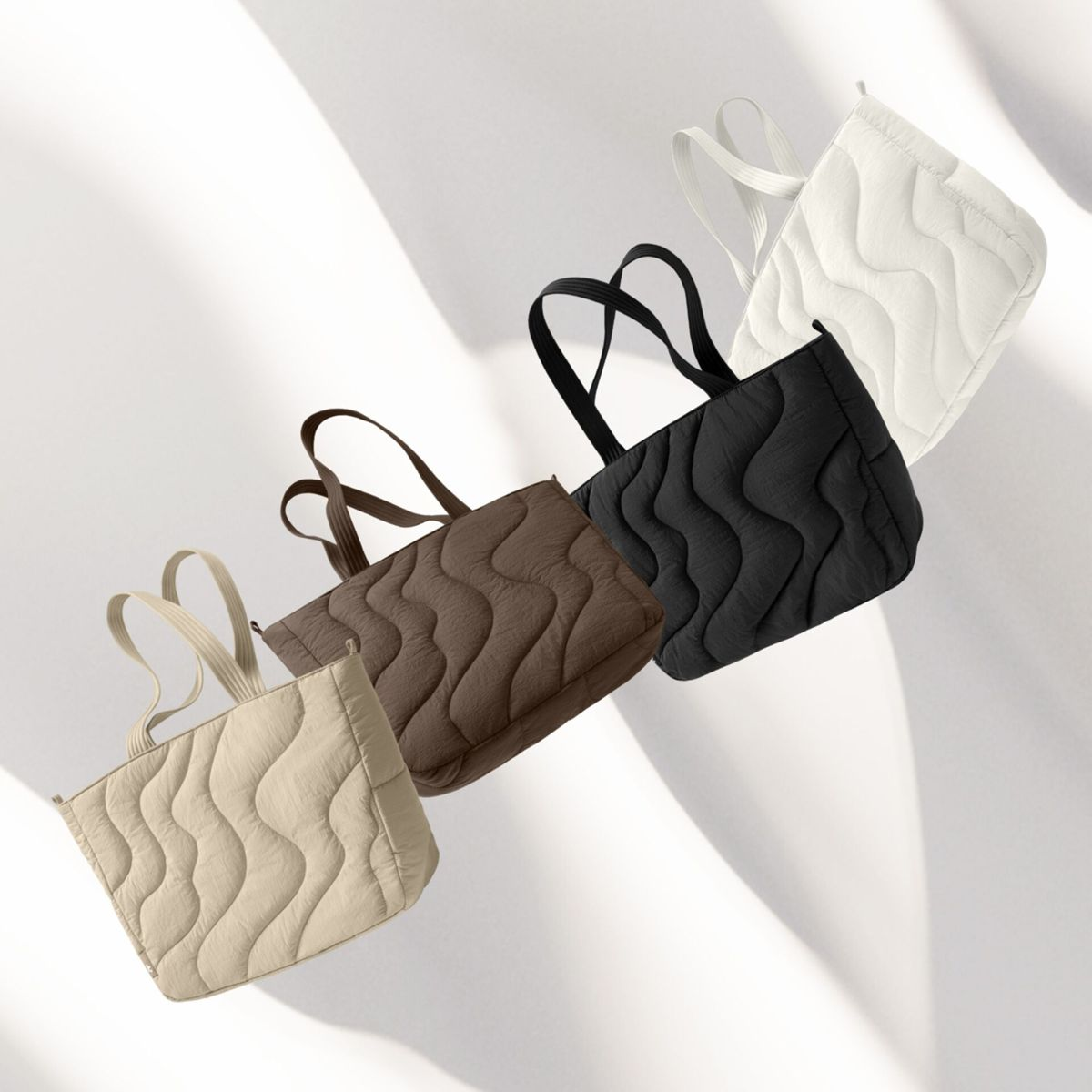 Vier gewatteerde tote tassen in beige, bruin, zwart en wit op witte achtergrond.