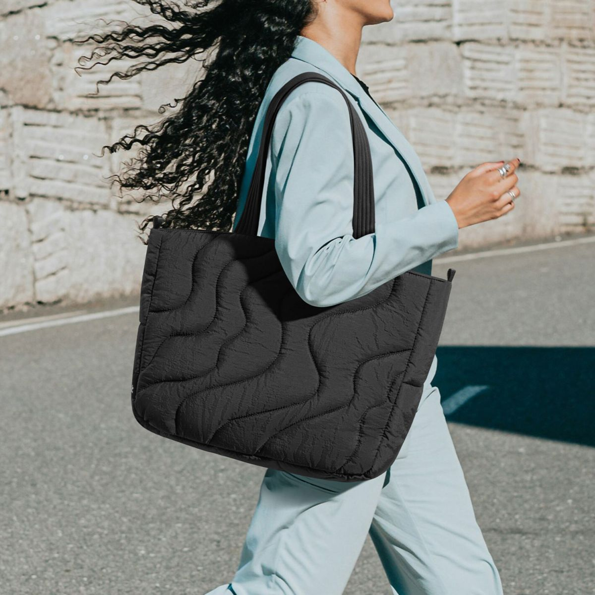 Una donna in tailleur azzurro cammina con una grande borsa trapuntata nera.
