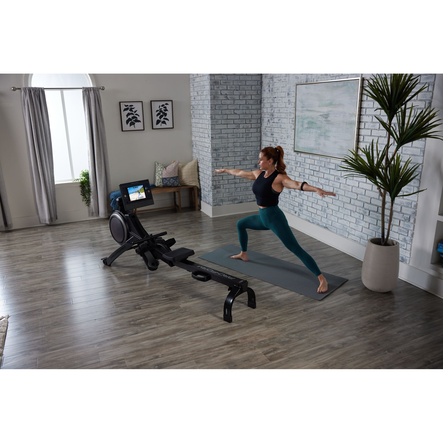 Eine Frau macht Yoga auf einer Matte neben einem Rudergerät in einem hellen Raum.