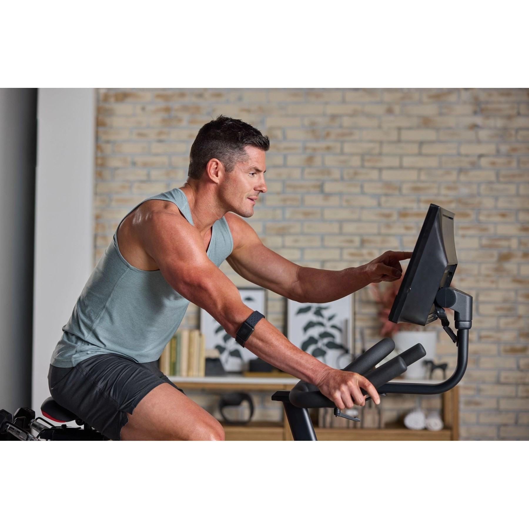 Ein Mann im Tanktop trainiert auf einem Heimtrainer vor einem Backsteinhaus.