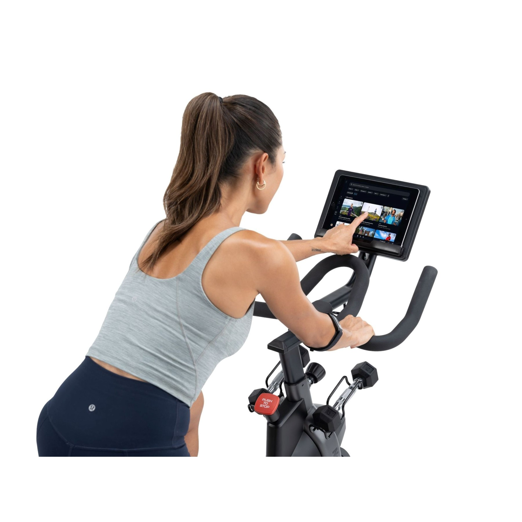 Eine Frau mit Pferdeschwanz trainiert auf einem Heimtrainer und tippt auf den Bildschirm.