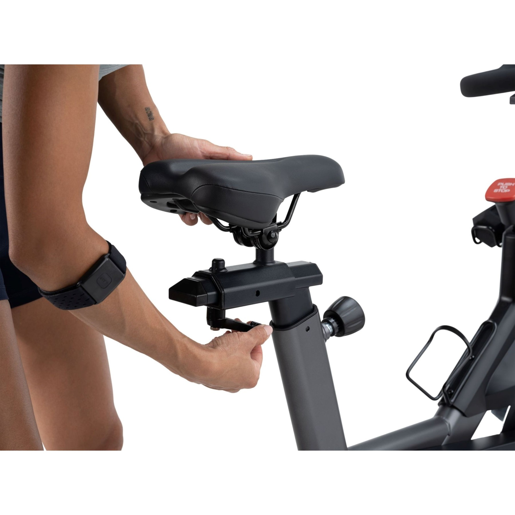 Eine Person passt den Sitz eines Heimtrainers an. Ein Armband ist am linken Arm zu sehen.