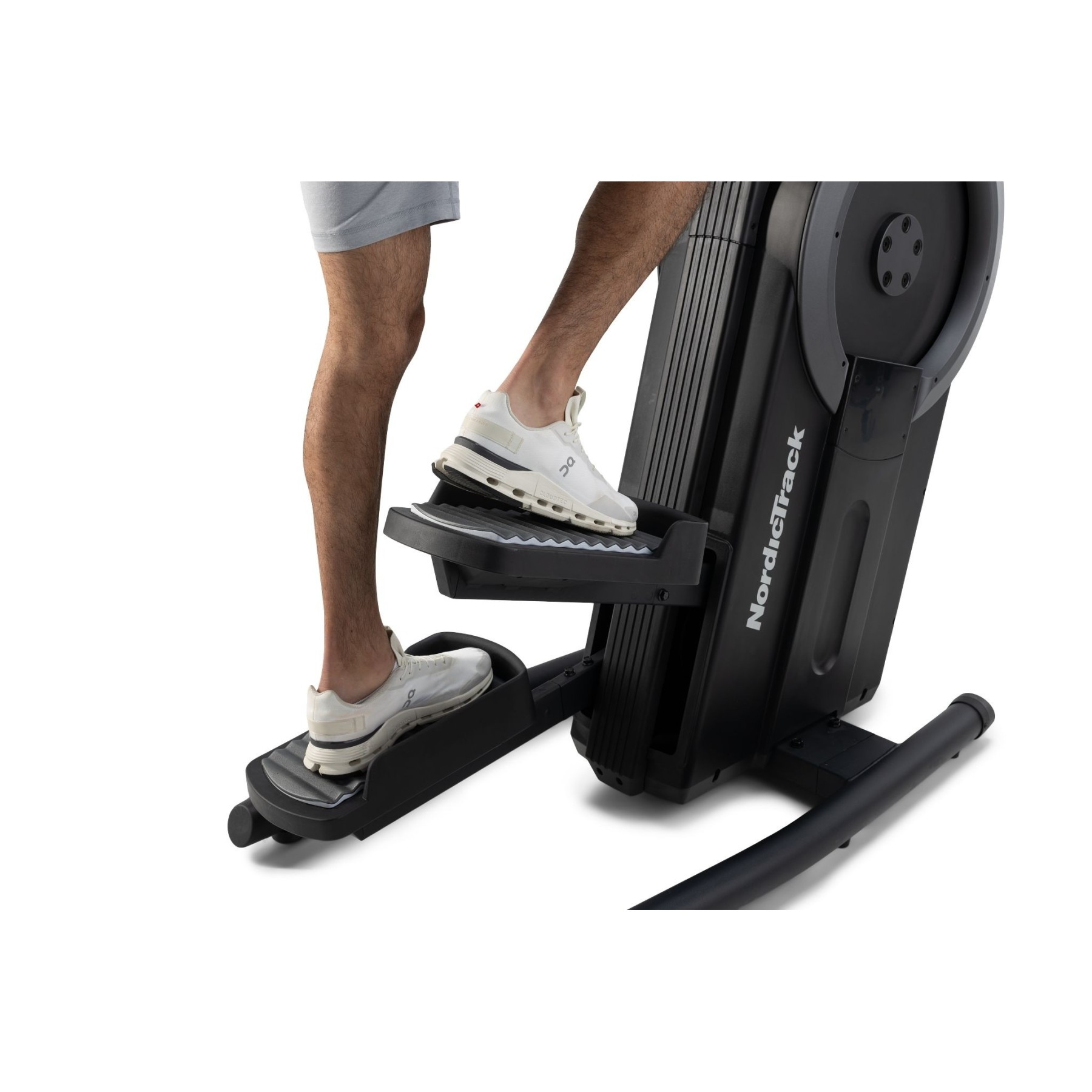 Ein Mann in grauer Hose und weißen Schuhen trainiert auf einem schwarzen Crosstrainer.