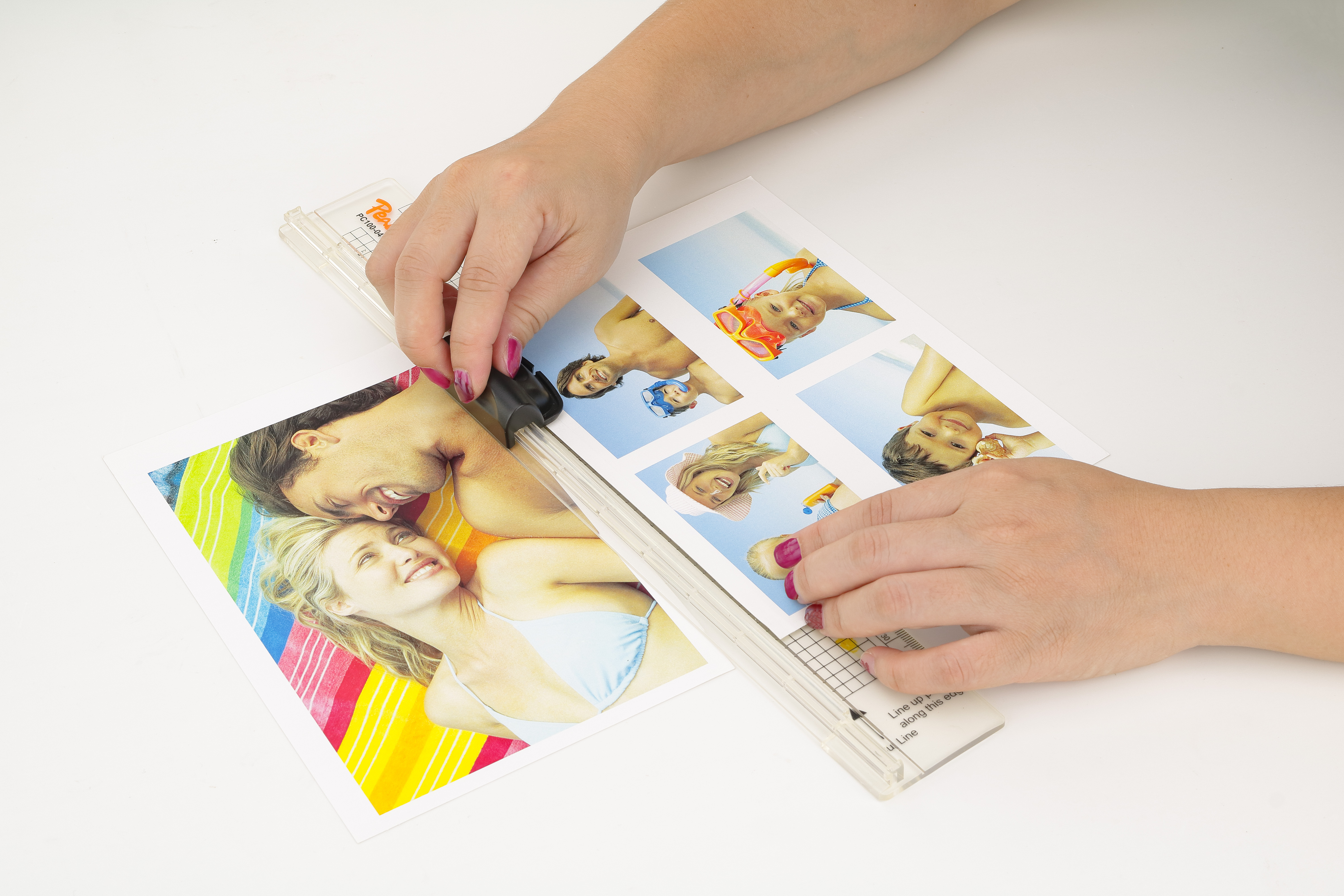 Hände schneiden Urlaubsfotos mit einem Papierschneider. Ein Paar liegt auf einem bunten Handtuch.