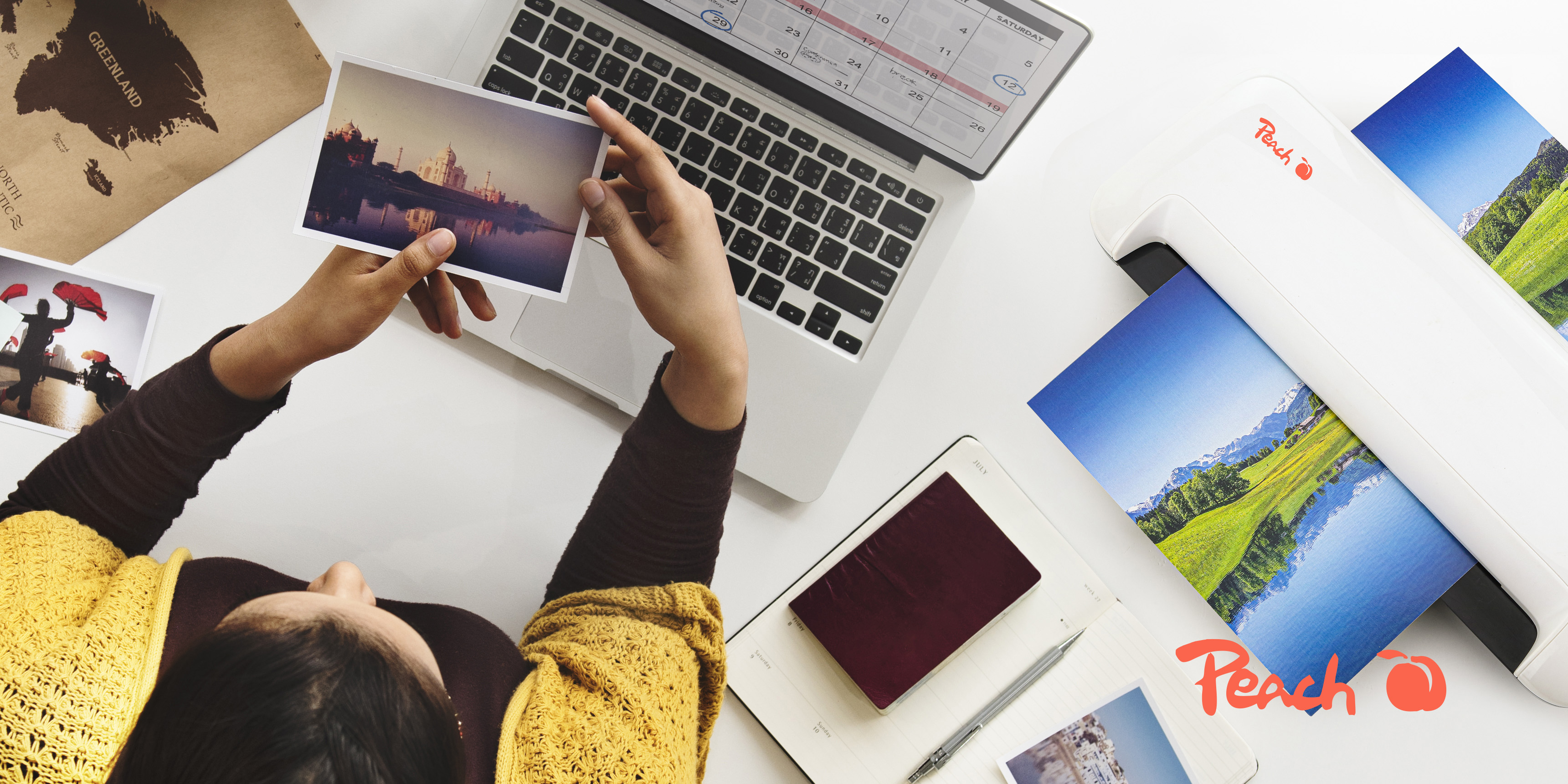 Une personne tient une photo du Taj Mahal, un ordinateur portable et une plastifieuse sur un bureau.