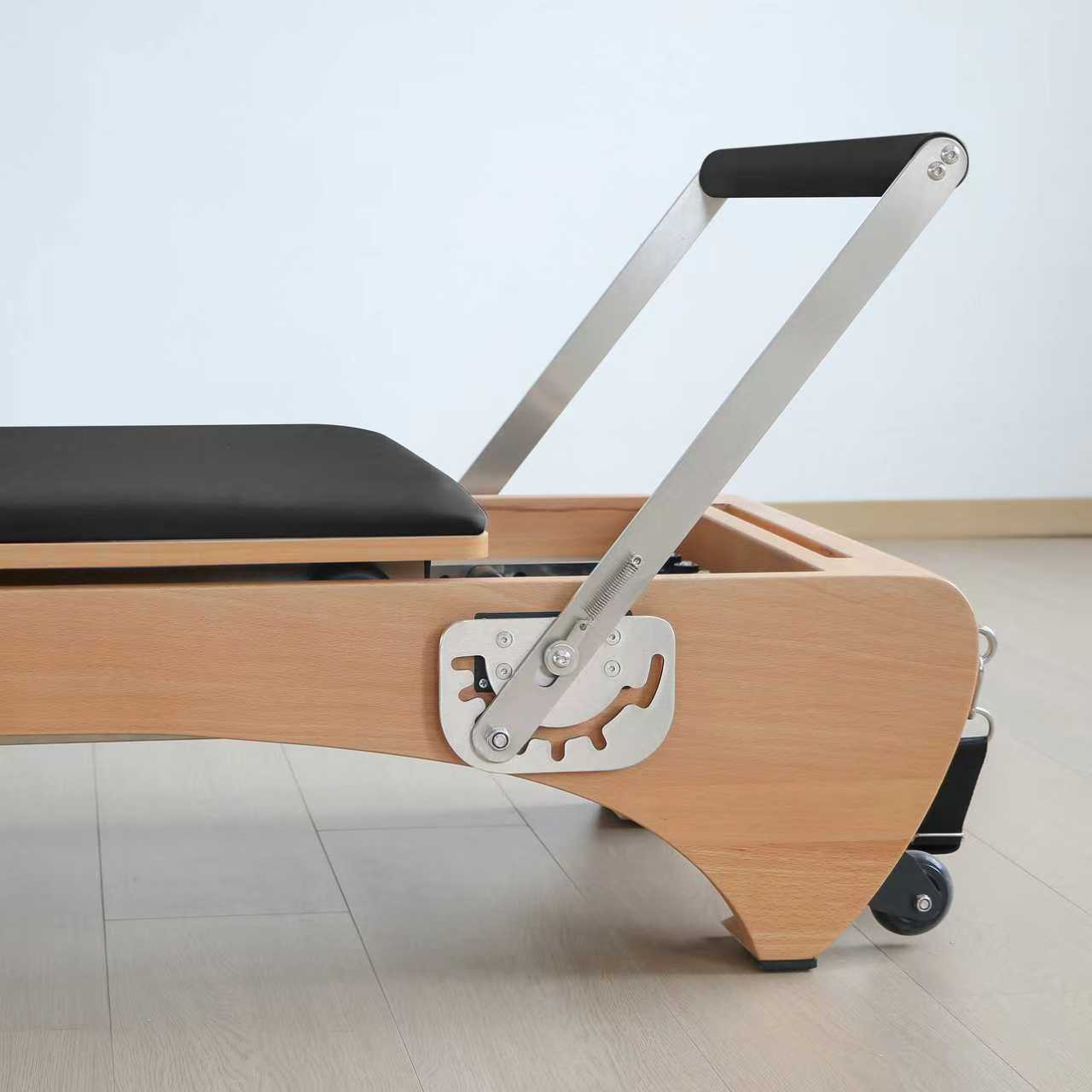 Ein Pilates-Reformer mit Holzrahmen, schwarzem Sitz und Metallgriffen.