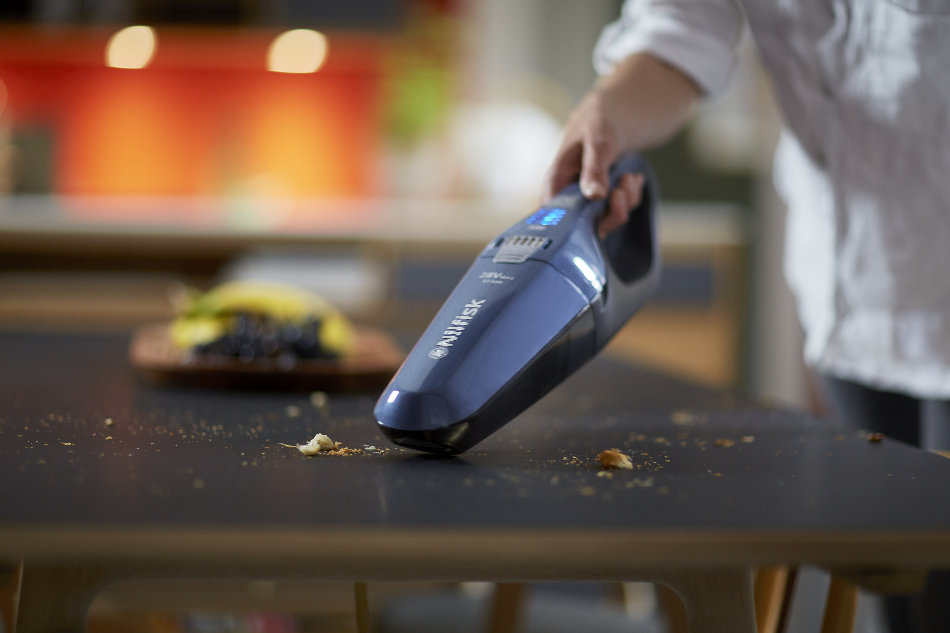 A blue handheld vacuum cleaner is used to clean crumbs from a table.