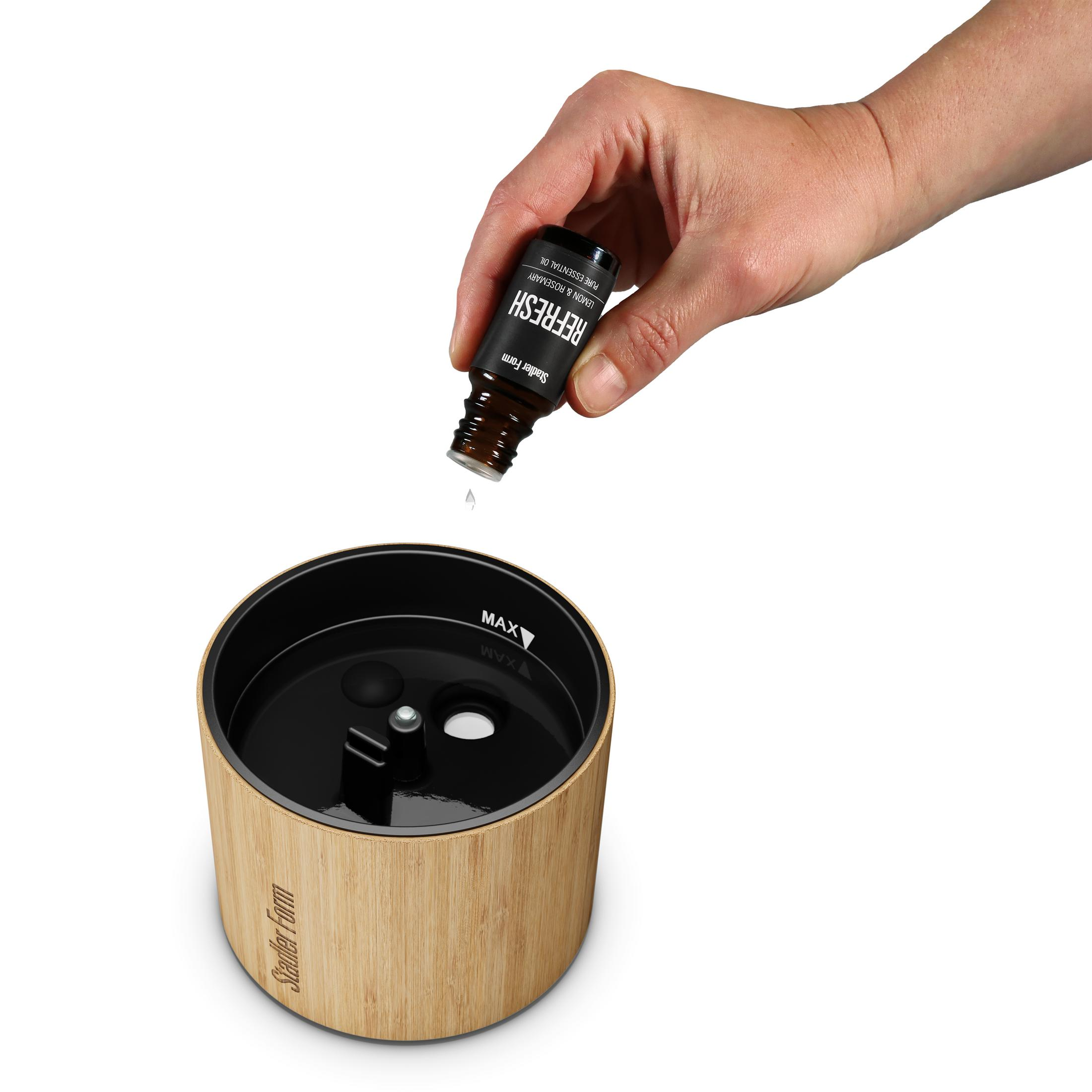 A hand drips essential oil into a diffuser with a bamboo casing.