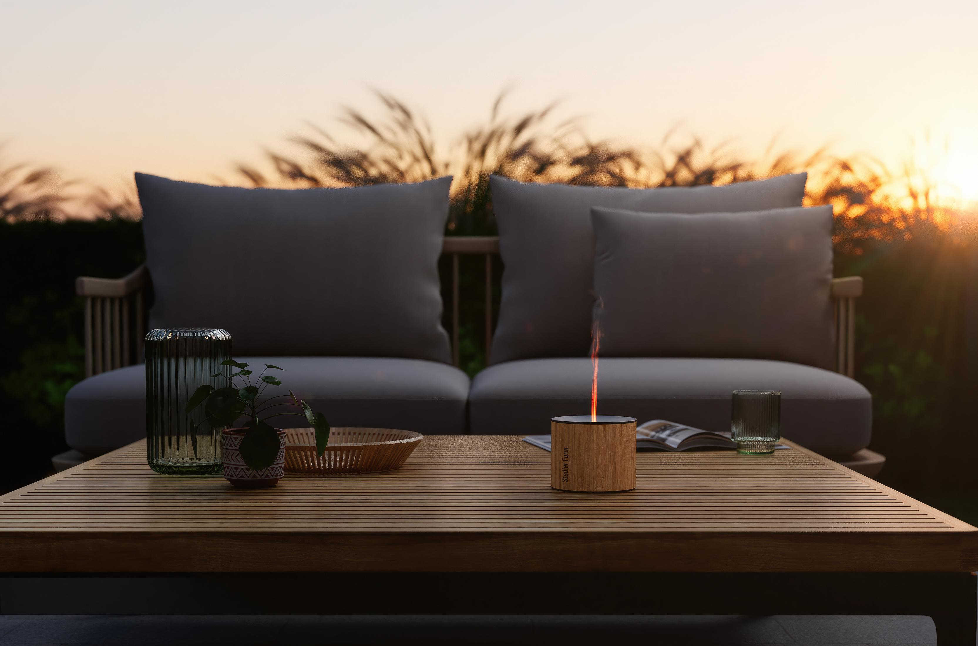 A table with decor, seating, and a small burning object at sunset.