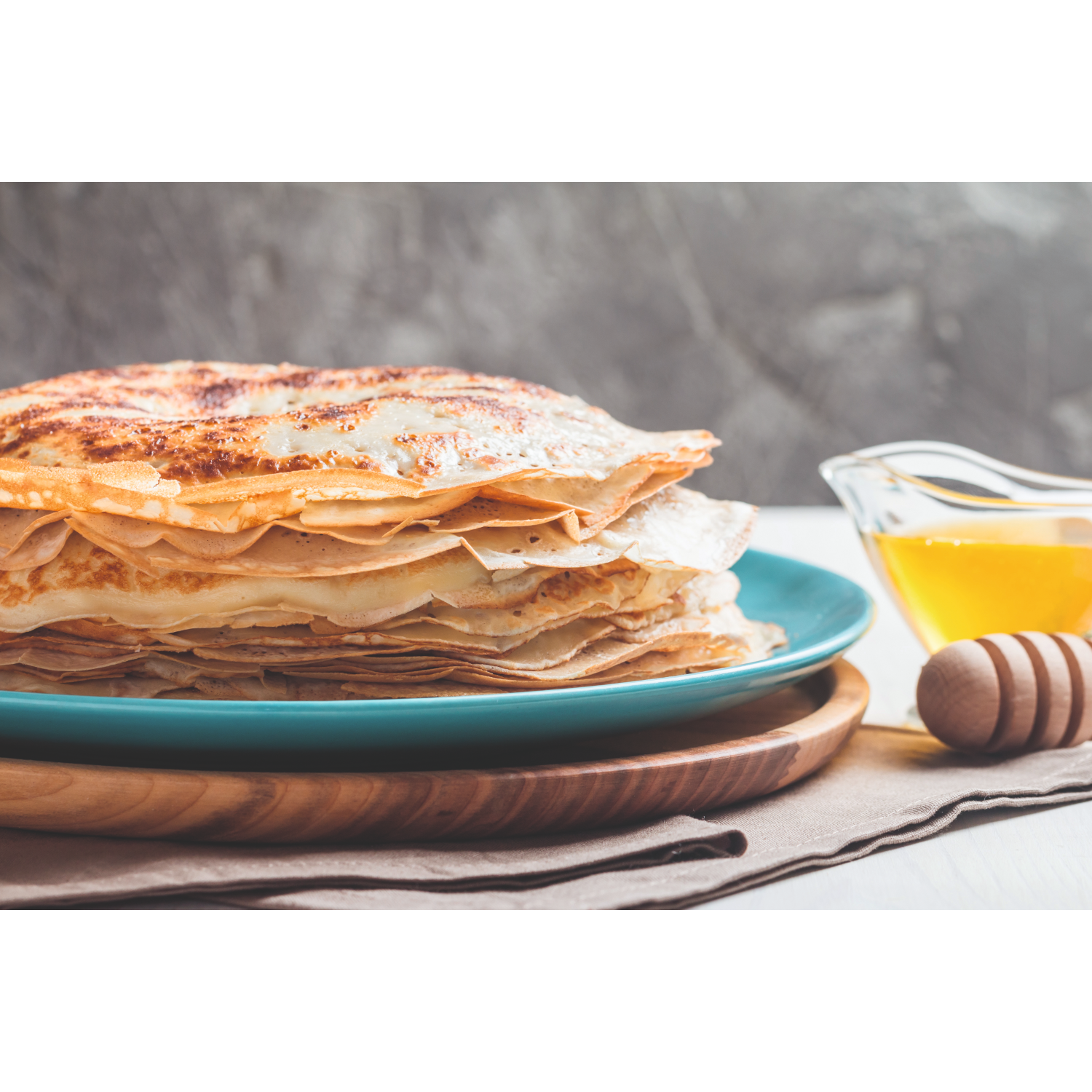 A stack of golden-brown pancakes on a blue plate with honey beside them.