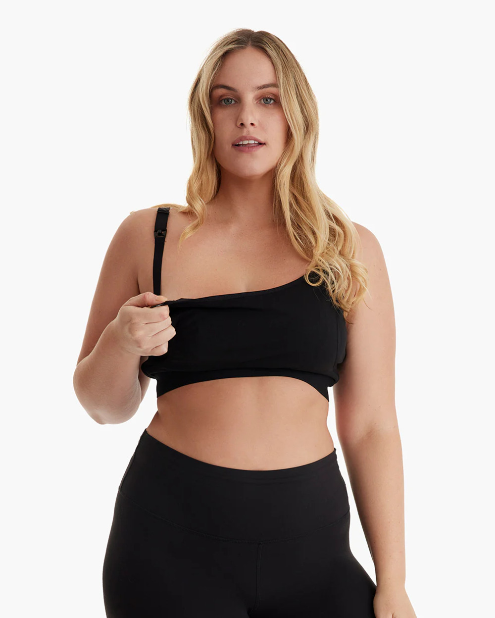 Una mujer rubia con sujetador deportivo negro y leggings. Se está tocando el sujetador.
