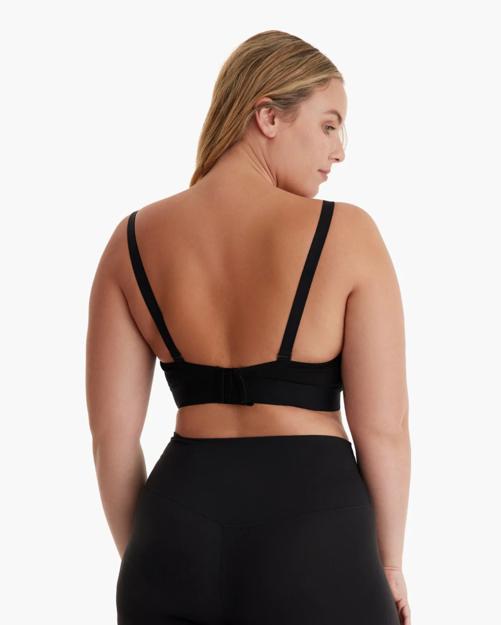 Vista trasera de una mujer rubia con sujetador deportivo negro y leggings.