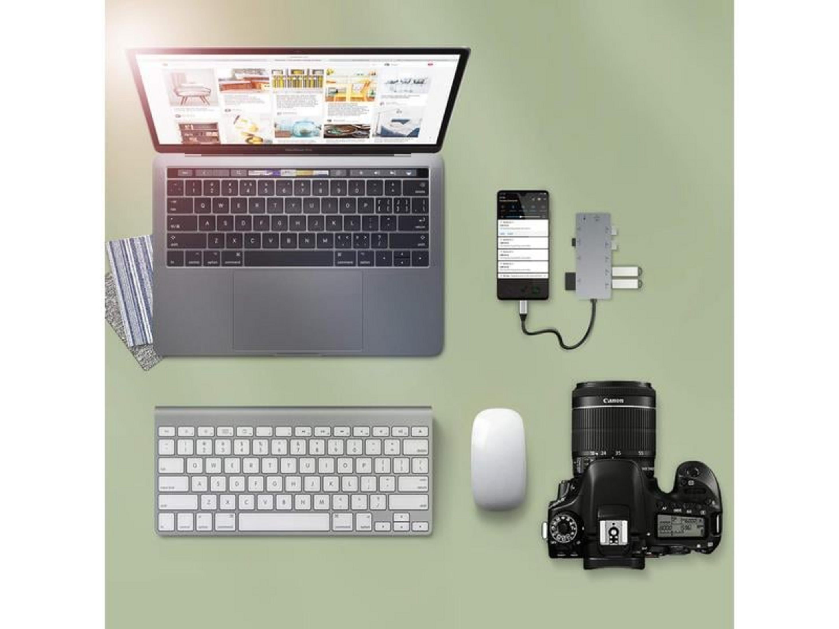 Un laptop, tastiera, mouse, telefono, hub USB e una fotocamera su sfondo verde.