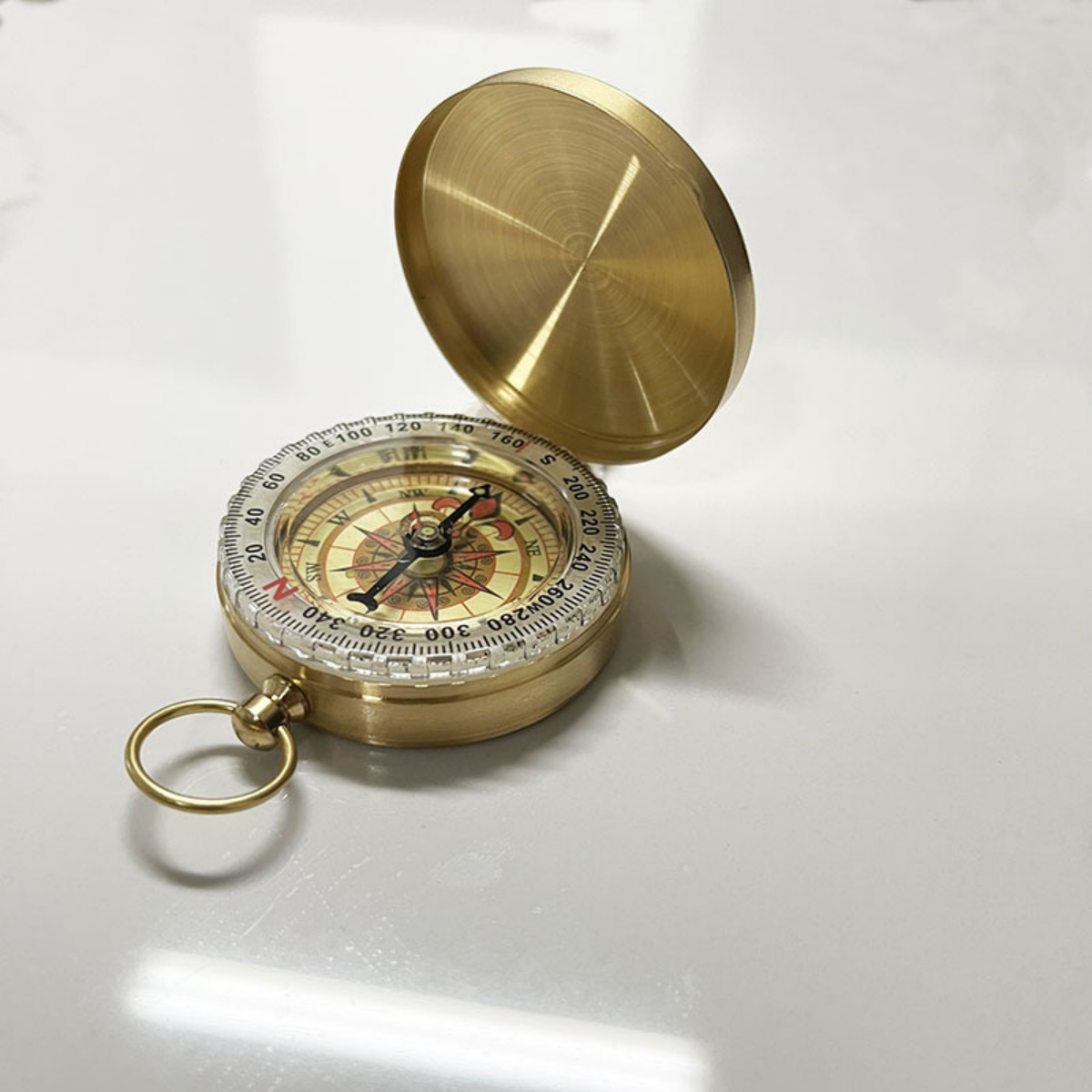 Eine goldene Messingkompass mit geöffnetem Deckel steht auf einer weißen Oberfläche.