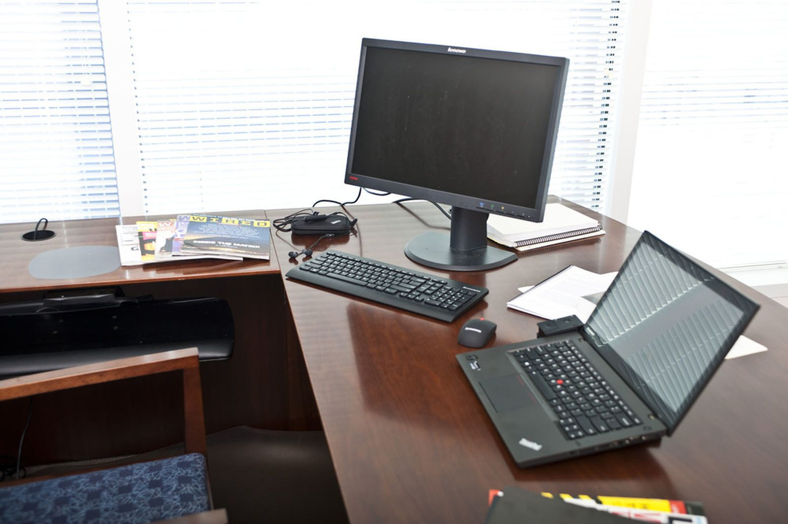 Una scrivania con laptop, monitor, tastiera, mouse e riviste.