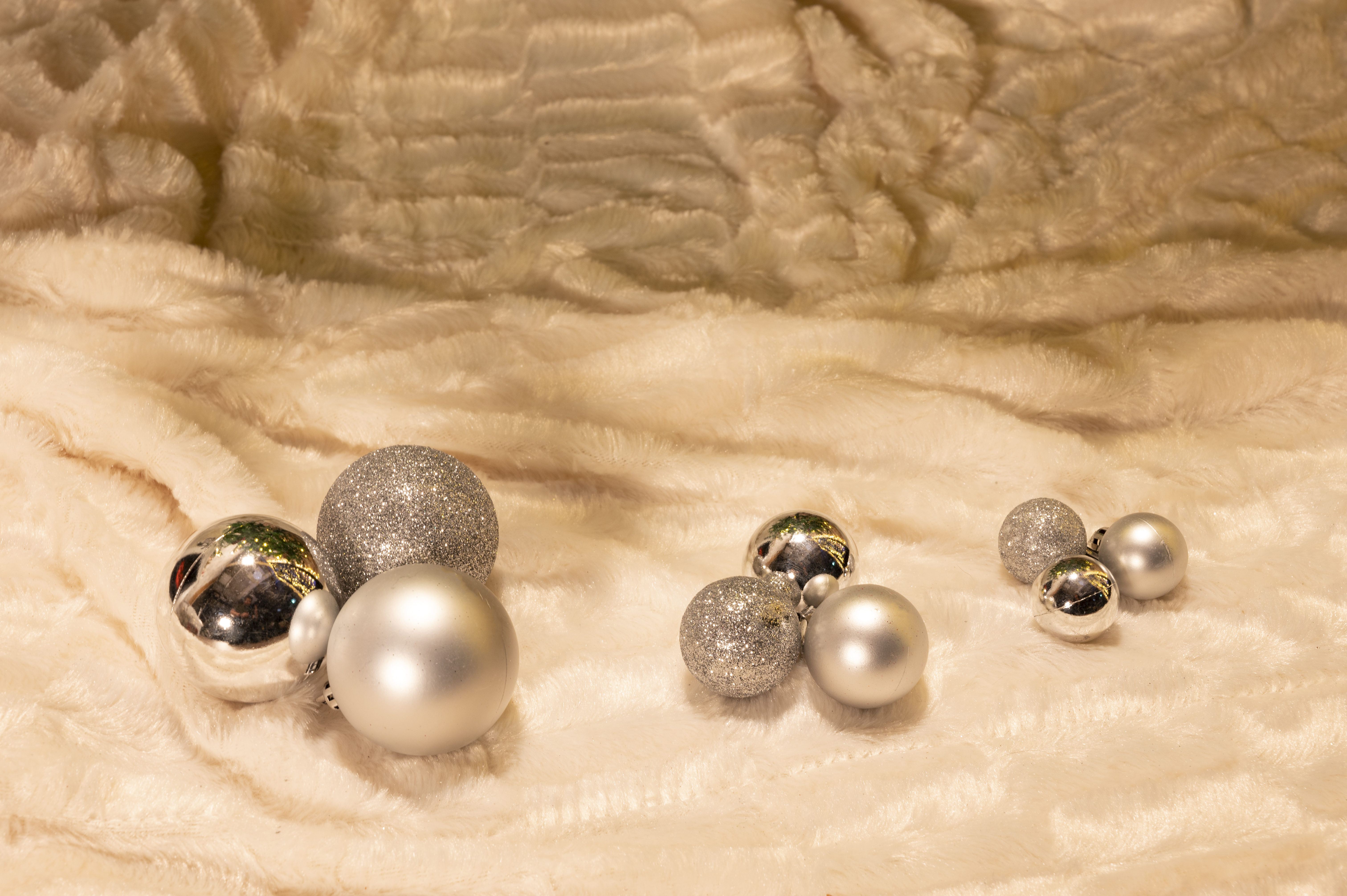 Zilveren en glitter kerstballen op crèmekleurige, pluizige stof.
