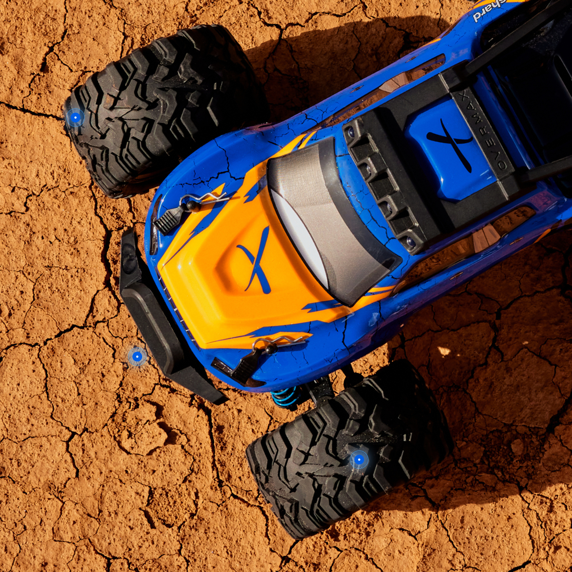 Ein blau-oranger ferngesteuerter Monstertruck sitzt auf rissiger trockener Erde.