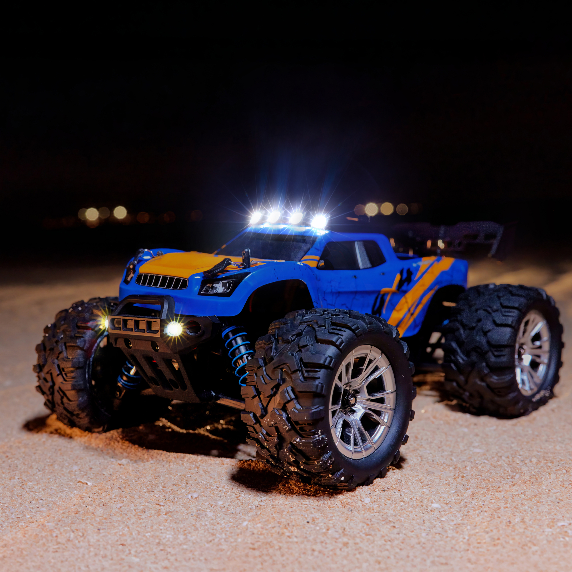 Ein blau-gelbes RC-Monster-Truck-Spielzeug mit Lichtern auf Sand im Dunkeln.
