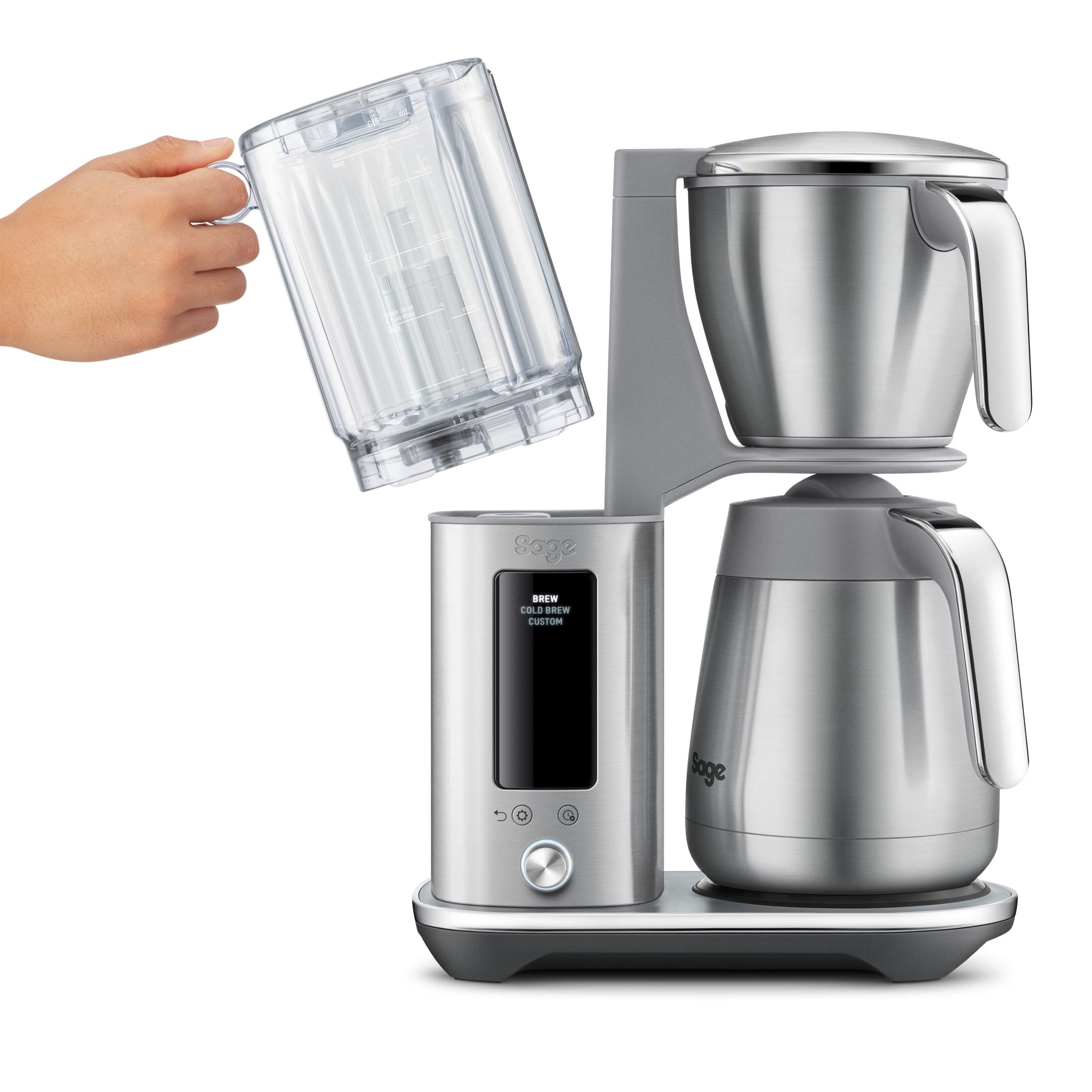 Una mano tiene una caraffa trasparente sopra una macchina da caffè Sage argentata con display digitale.
