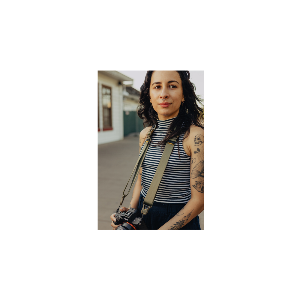 Vrouw met tatoeages, gestreept topje, houdt camera vast. Buiten.