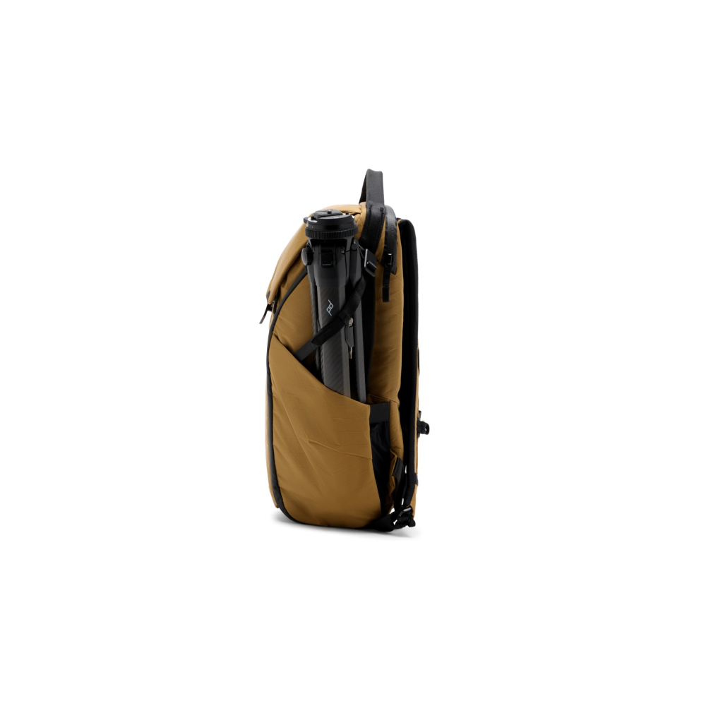 A tan backpack with a black tripod secured in a side pocket.