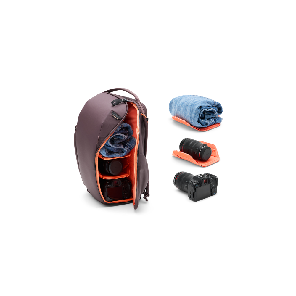 A purple backpack is open, showing clothes and camera gear. Separate items include jeans, a lens, and a camera.