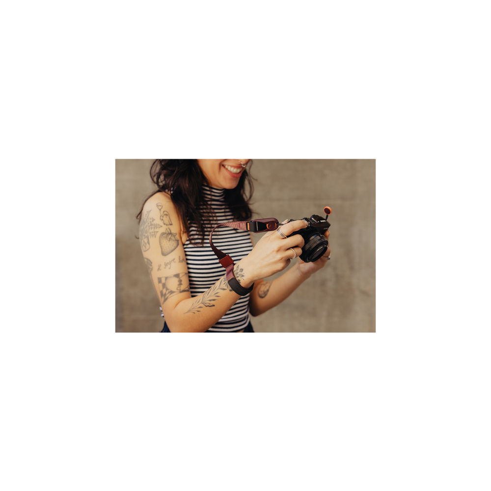 A tattooed woman holds a camera, wearing a striped top.