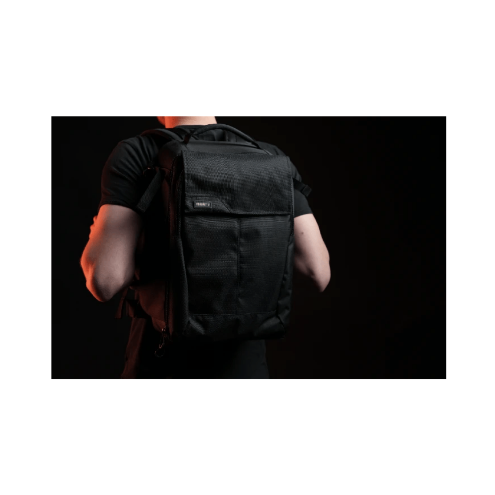 A man wears a black backpack with red light from the side.