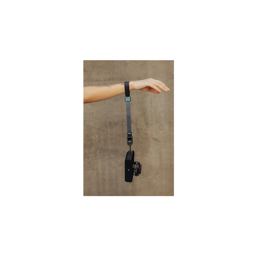Een hand houdt een camera aan een riem voor een betonnen muur.