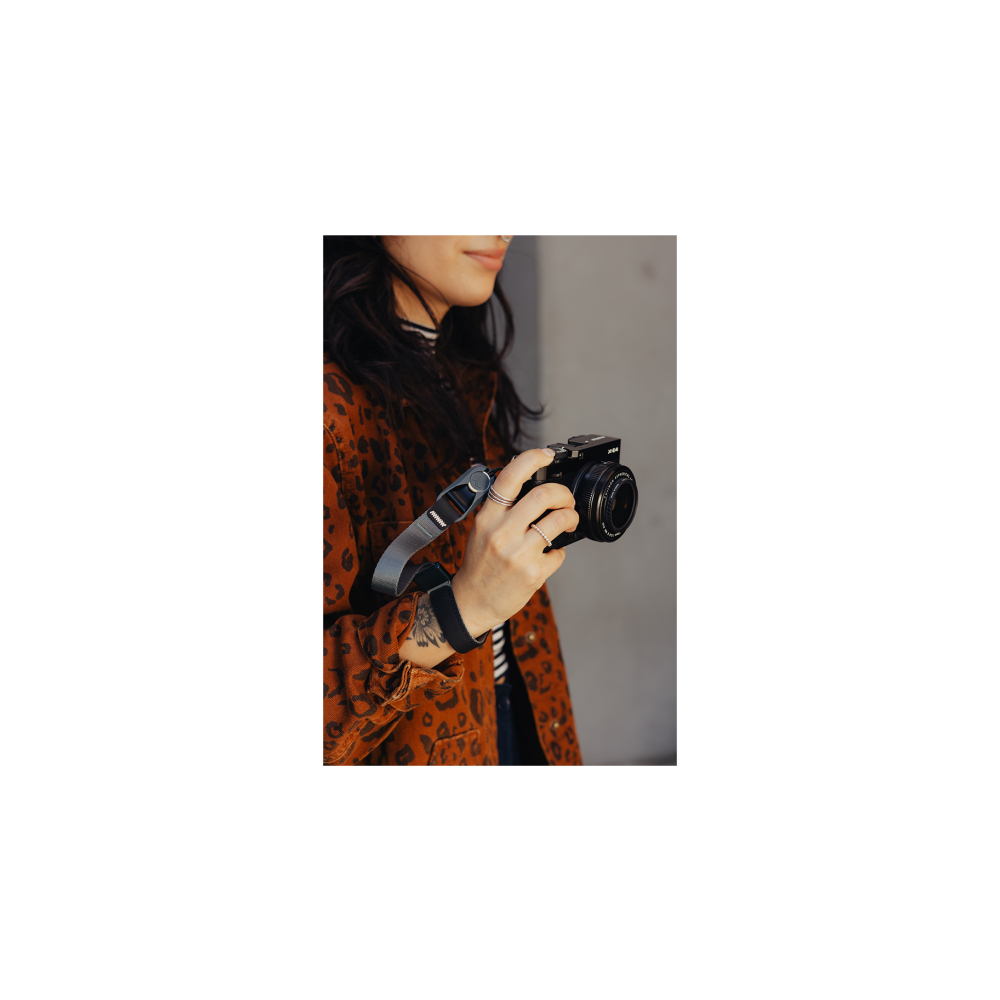 Een vrouw houdt een zwarte camera vast, draagt een jas met luipaardprint.