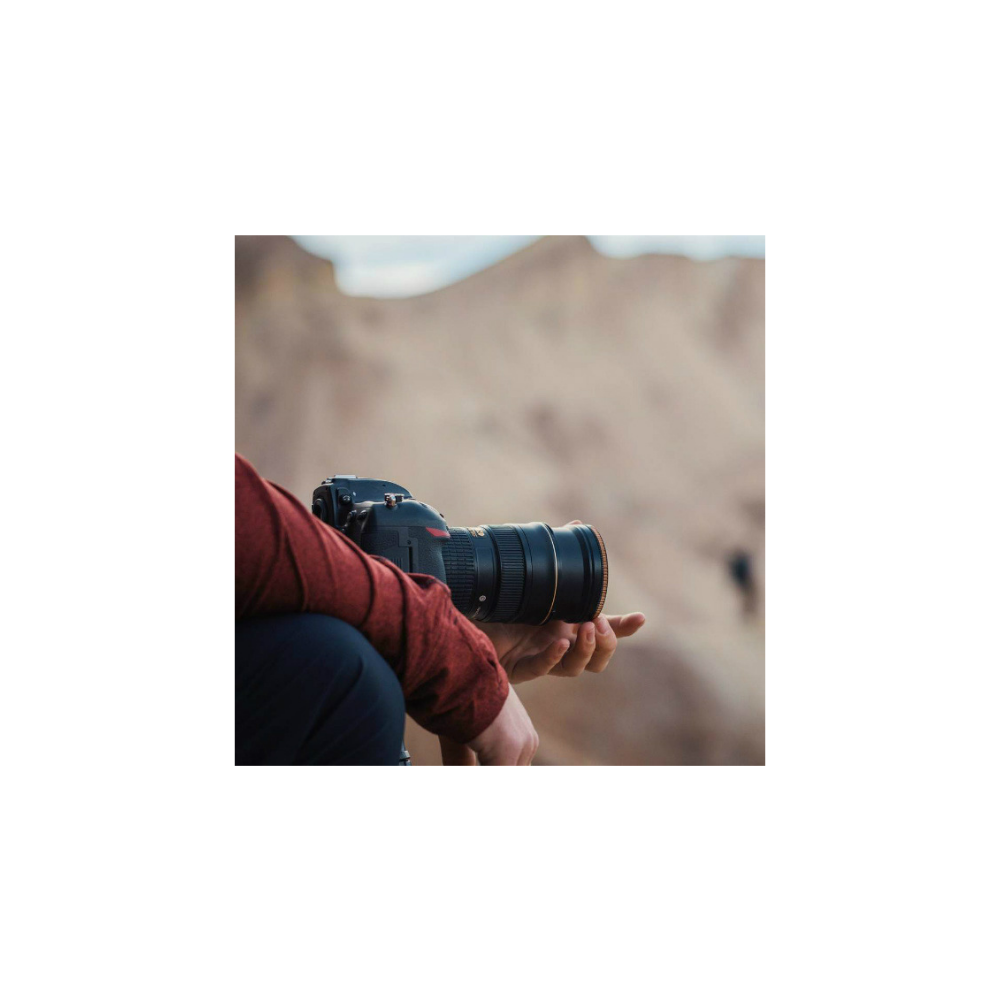 Een persoon in een rood shirt hurkt en houdt een camera met een grote lens vast.