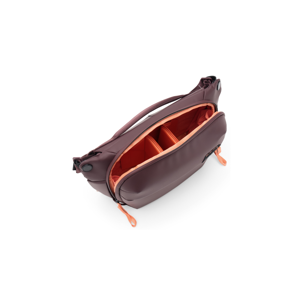 Een bordeauxrode tas met een oranje interieur, liggend op een witte achtergrond.