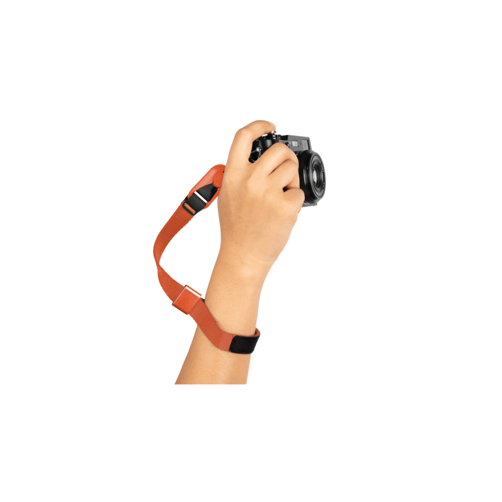 Een hand houdt een zwarte camera vast met een oranje band om de pols.