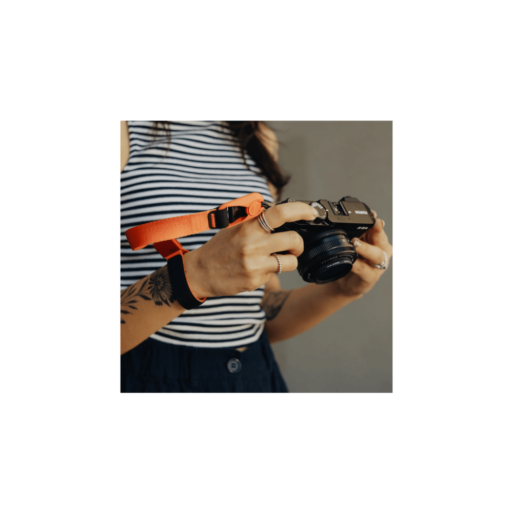 Een persoon met een oranje camerariem die een camera vasthoudt.