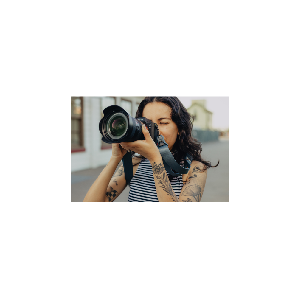 Een getatoeëerde vrouw maakt een foto met een camera. Ze draagt een gestreepte top.
