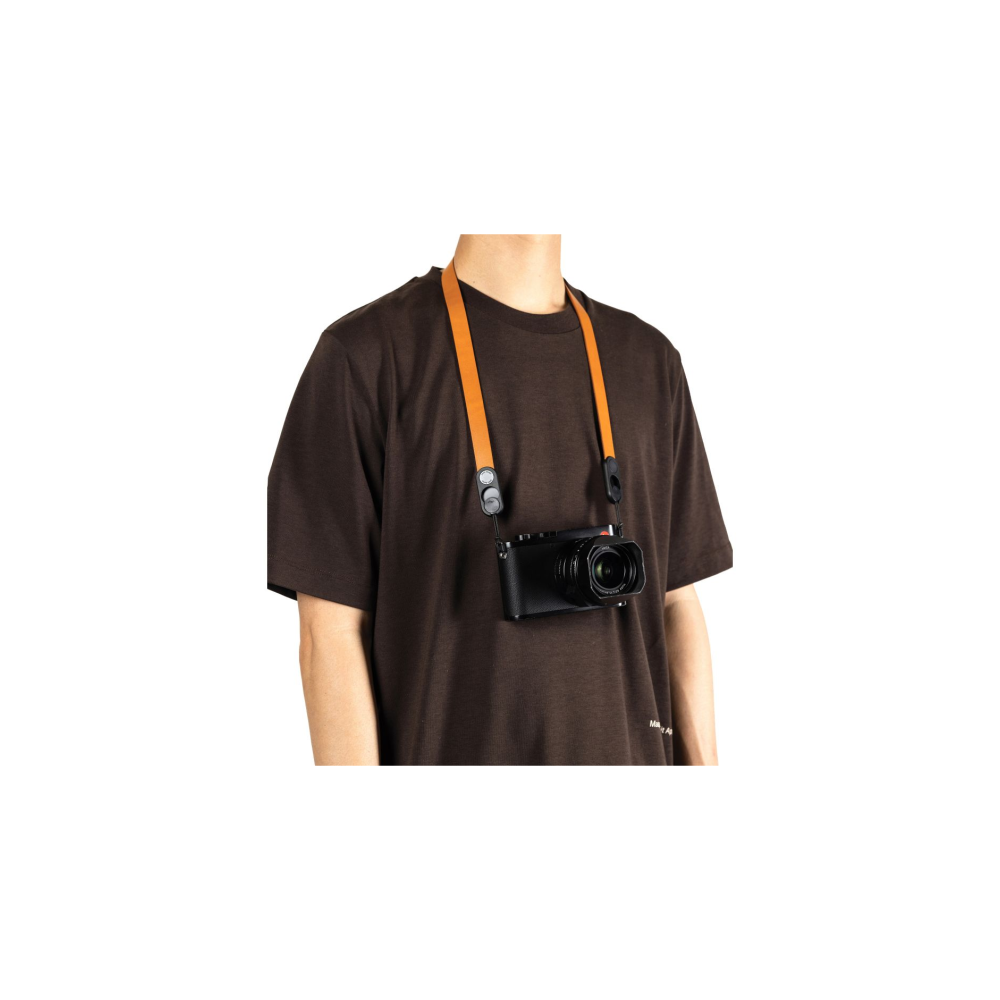 Persoon in bruin t-shirt met oranje camerariem en zwarte camera.