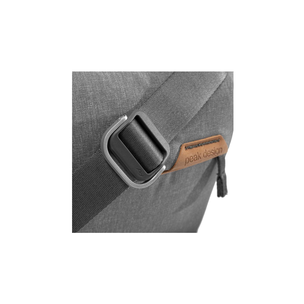 Grijze rugzak met zilveren riemclip en bruin leren label met tekst Peak Design.