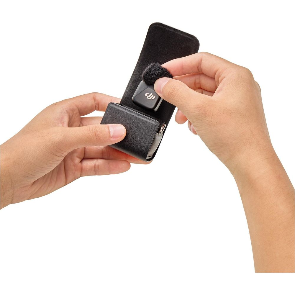 Hands placing a black DJI microphone with a fuzzy windscreen into a black case.
